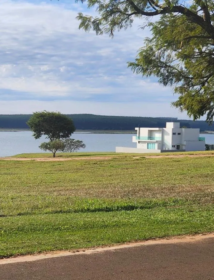 Lote gramado de frente para a represa, com uma casa branca ao fundo